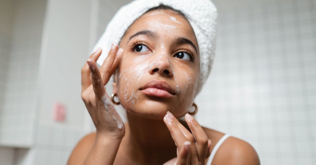 A young woman applies skincare cream in a modern bathroom setting.